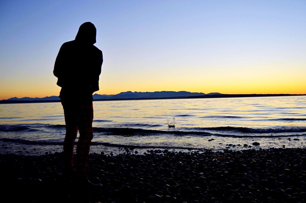 SILHOUETTE MAN STANDING AT BEACH AGAINST CLEAR SKY