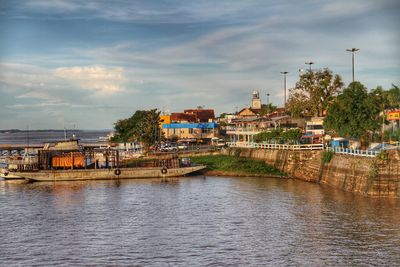 Buildings by river against sky in city