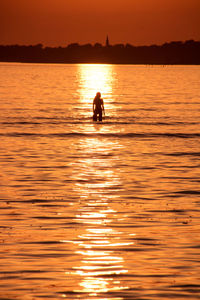 Silhouette person swimming in sea against sky during sunset