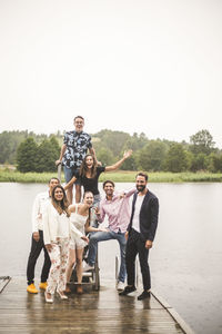 Portrait of cheerful multi-ethic friends standing on jetty over lake during holiday