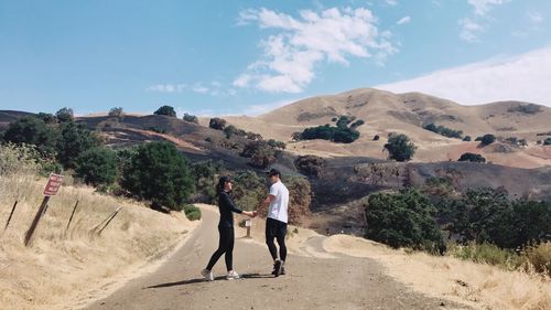 Full length of people standing on road against mountains during sunny day