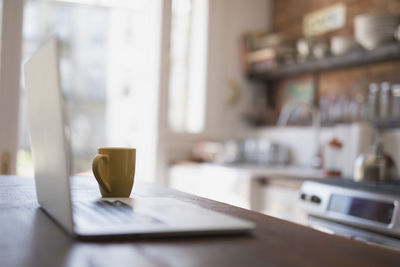 Coffee cup and laptop on kitchen counter