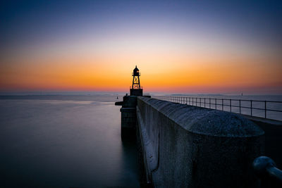 Lighthouse on pier by sea against sky during sunset