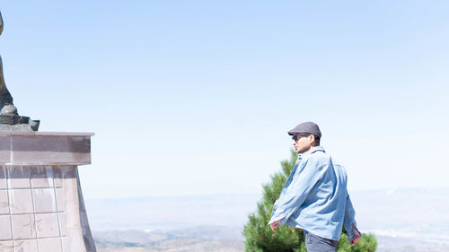 Side view of young man looking at view against clear sky