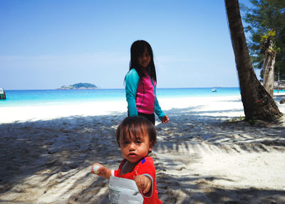 Siblings at beach against sky