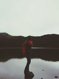 Reflection of woman on puddle at beach against clear sky