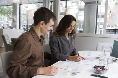 Man looking at woman smiling while signing agreement at desk in real estate office