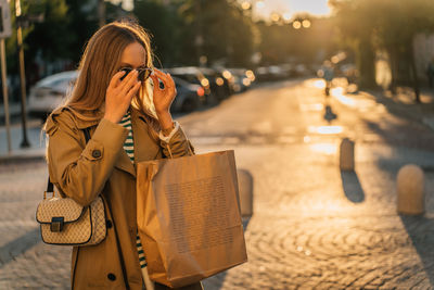 A woman walks around the city after shopping at sunset with a paper bag