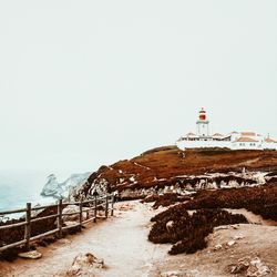 Lighthouse by sea against foggy sky