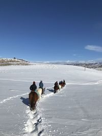 People horseback riding on snowy field against blue sky