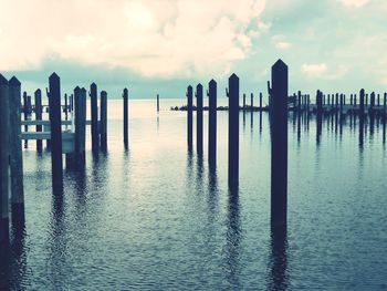 Wooden posts in sea against sky