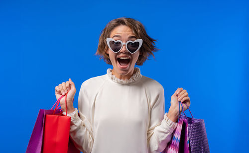 Portrait of woman wearing sunglasses while standing against blue sky