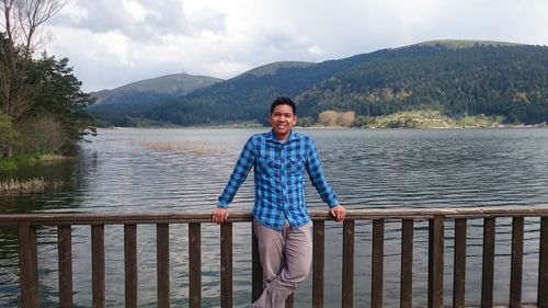 Portrait of young man standing by railing against lake