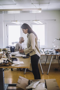 Side view of female fashion designer writing on package while working at workshop