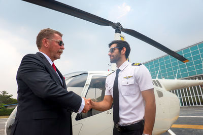 Businessman shaking hand with pilot by helicopter