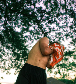 Low angle view of shirtless man against branches at park