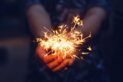 Midsection of person holding illuminated sparkler at night
