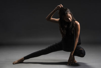 Full length of young woman exercising against black background