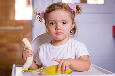 Cute baby girl with banana on high chair at home