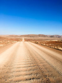 Road amidst desert land against blue sky