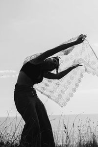 Silhouette young woman with scarf standing at beach against sky