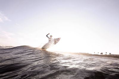 Low angle view of people splashing water in sea against sky