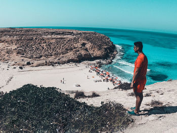 Full length of men standing on rock at beach against sky