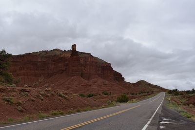 Road leading towards rock formation against sky