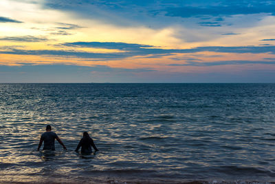 Silhouette people standing in sea against sky during sunset