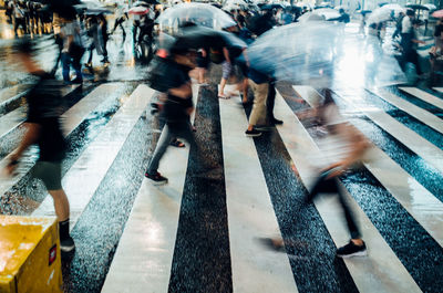 Blurred motion of people walking with umbrella on road