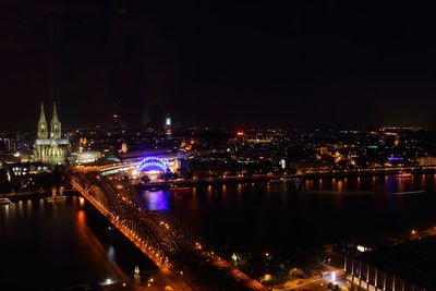 Illuminated hohenzollern bridge over rhine river by cologne cathedral against sky at night