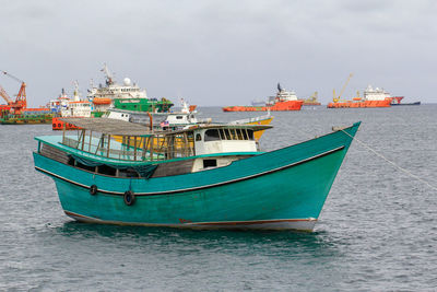 Fishing boats moored at harbor against sky