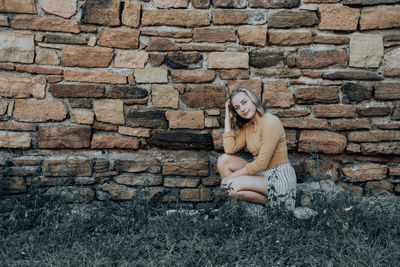 Portrait of smiling woman crouching against brick wall