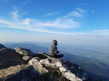 Man sitting on rock against sky