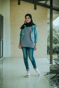 Full length portrait of young woman standing on tiled floor