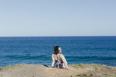 Rear view of woman sitting at beach against clear sky