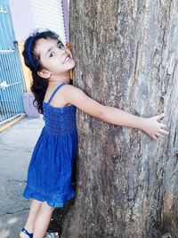 Portrait of cute girl embracing tree trunk