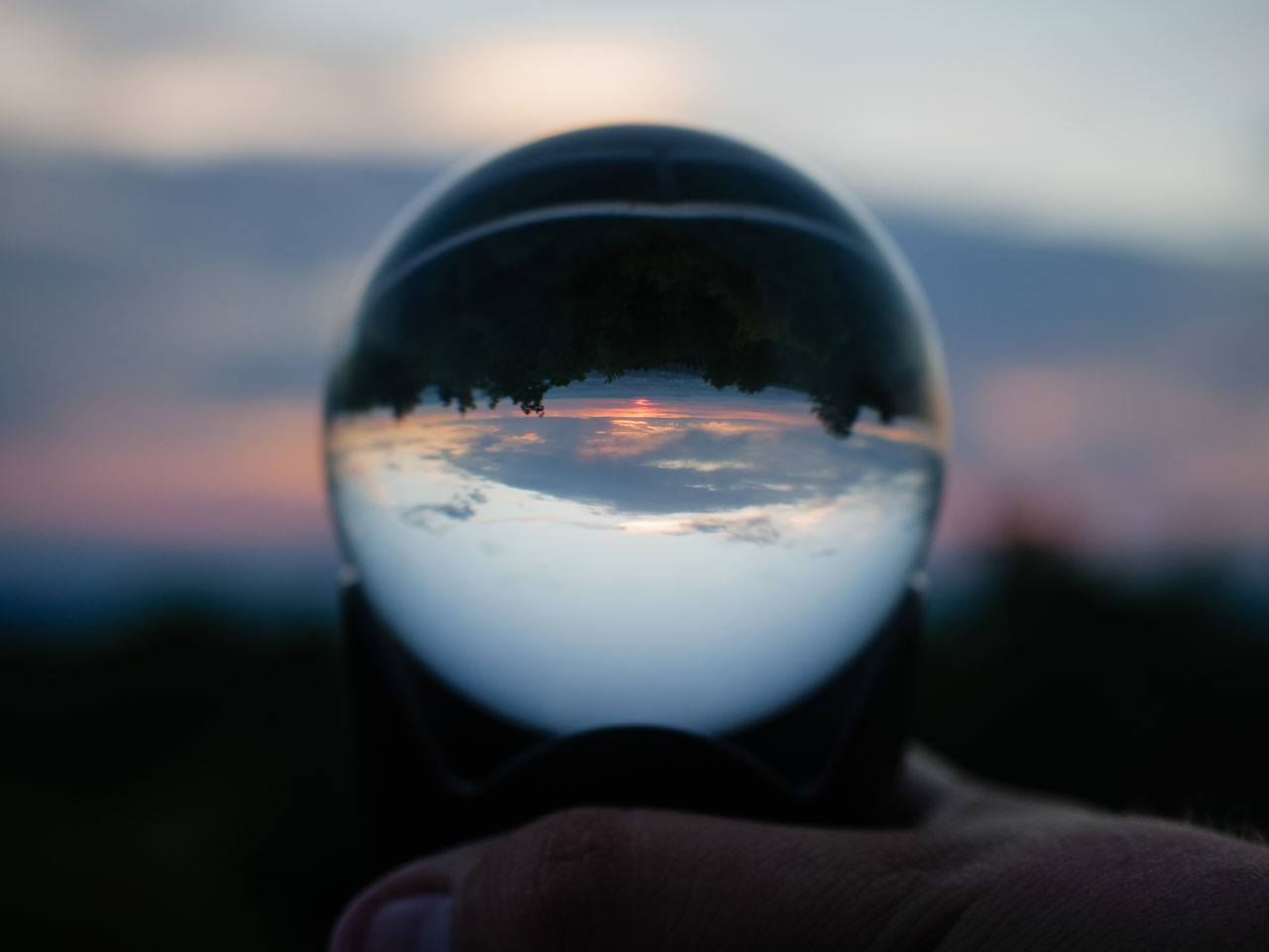 CLOSE-UP OF HAND HOLDING CRYSTAL BALL AGAINST SKY