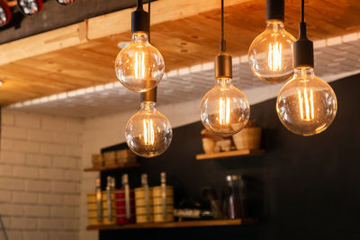 Close-up of illuminated light bulb hanging from ceiling