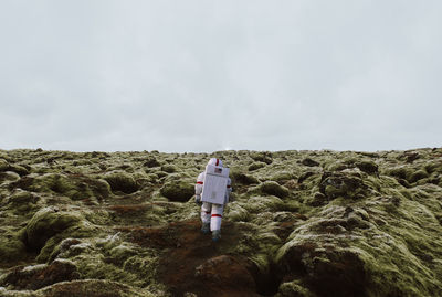 Rear view of man standing on rock against sky