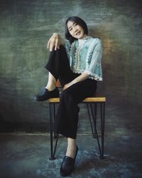 Portrait of woman sitting on chair against wall