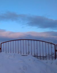 Fence on snow covered landscape against sky