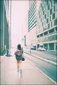 Rear view of woman walking on street against buildings in city