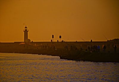 People fishing by sea against clear sky