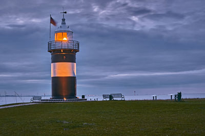 Lighthouse on field by building against sky