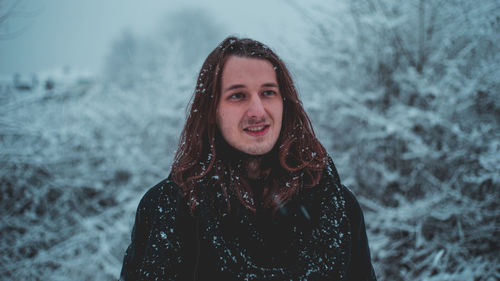 Smiling young man with snow on body standing in forest during winter