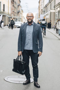 Full length of smiling mature businessman standing on city street