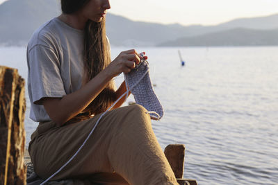 Young woman knitting in front of sea