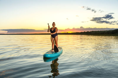 Rear view of man jumping in lake against sky during sunset