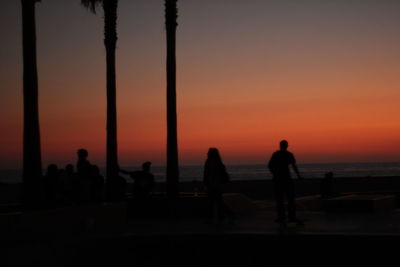 Silhouette people by sea against sky during sunset